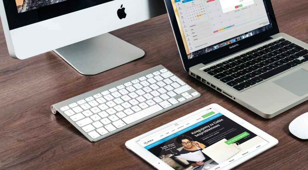 A sleek office desk setup featuring Apple devices: iMac, MacBook, and iPad.